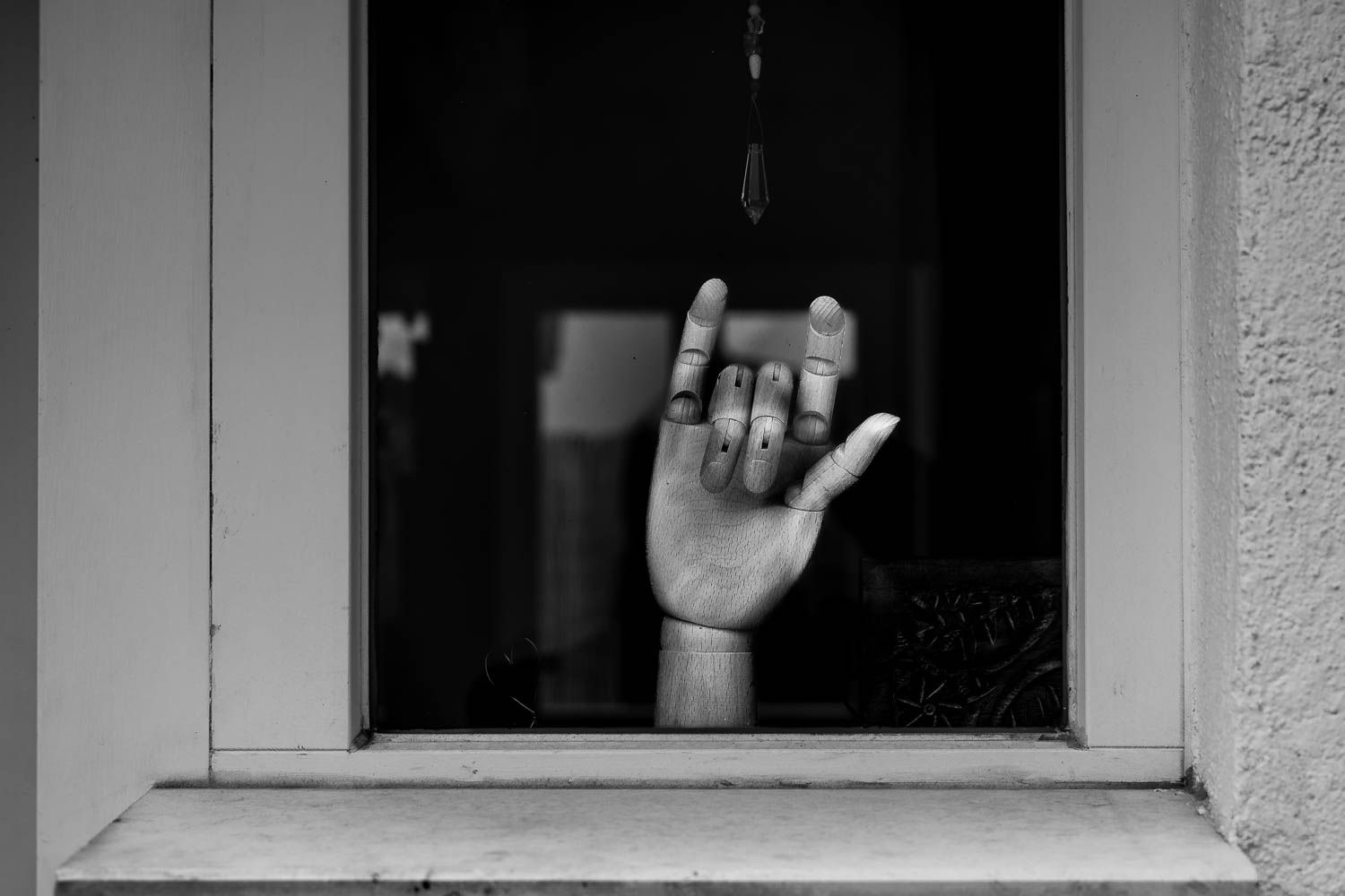 Eine hölzerne Hand mit beweglichen Fingergliedern steht in einem Fenster. Die Hand wurde so "konfiguriert", dass sie die "I love you" Geste zeigt. 🤟