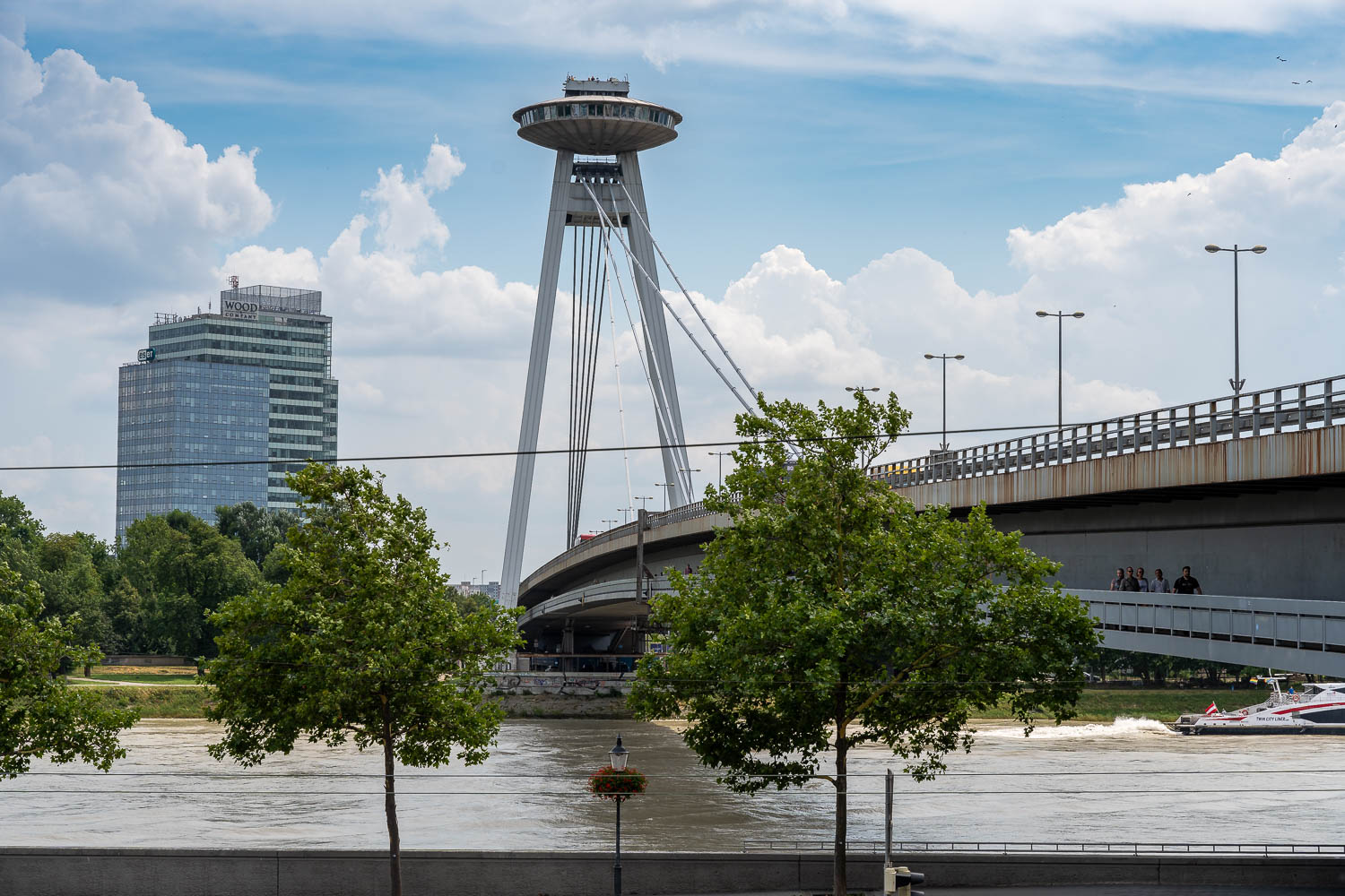 Blick entlang einer Donaubrücke. Oberhalb der Brücke ist auf Betonsäulen eine UFO-förmige Aussichtsplattform angebracht.