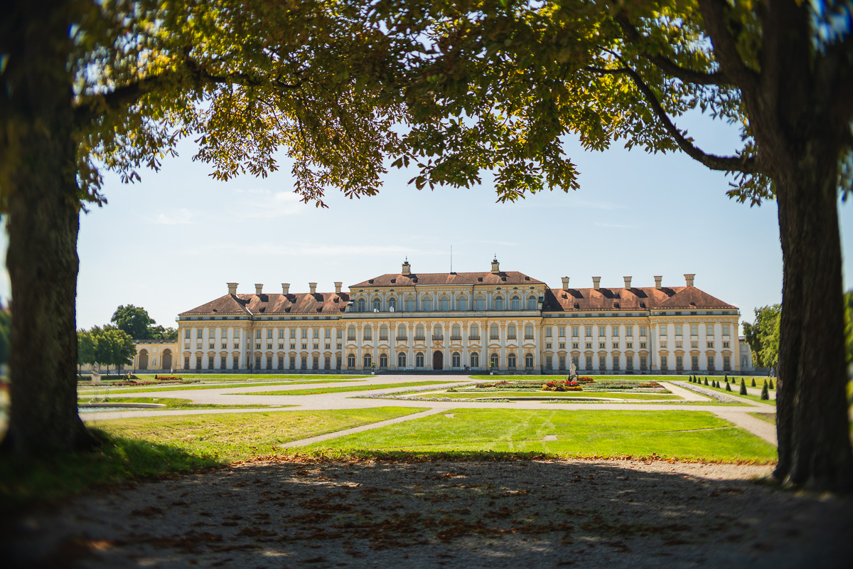 Großes lang gezogenes, historisches Gebäude von unterhalb einer Baumgruppe aufgenommen.