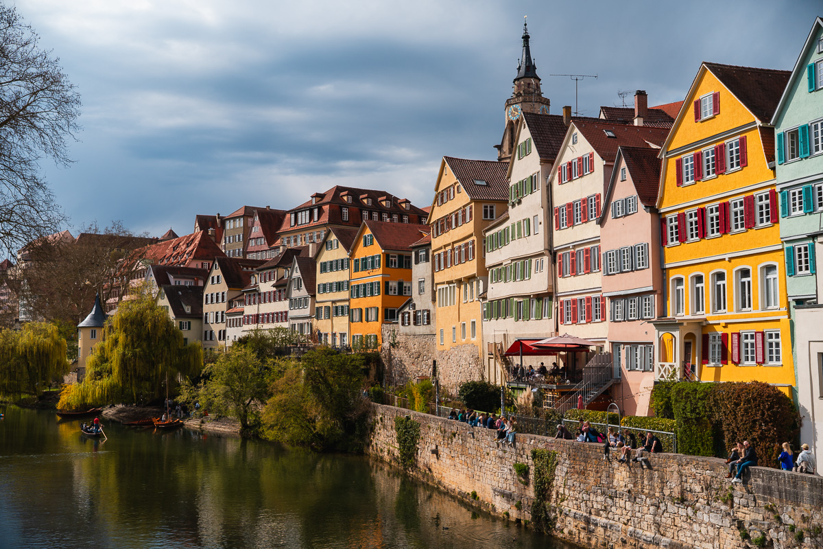Historische bunte Häuser stehen an einem Fluss. Im Hintergrund ein Kirchturm.